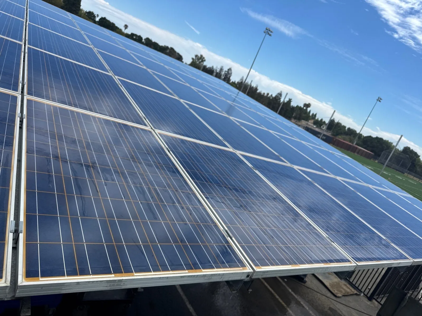 School district solar carport panels with visible water streaks from cleaning, next to a sports field, Pittsburg CA
